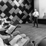 Black and white shot of students taking notes during a lecture in a modern hall.