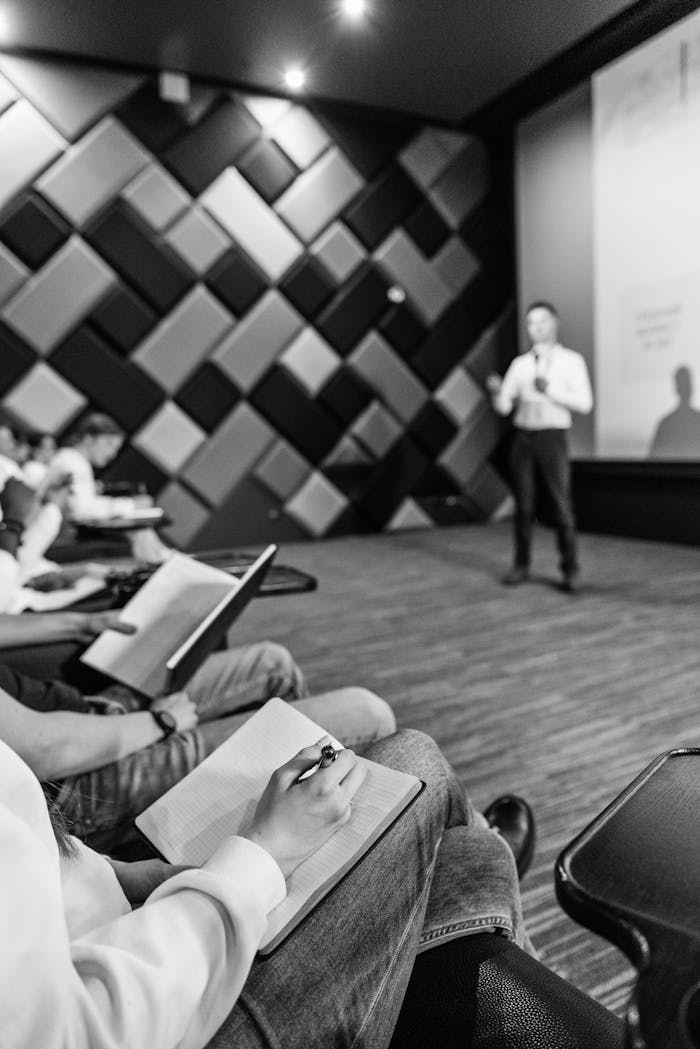 Black and white shot of students taking notes during a lecture in a modern hall.