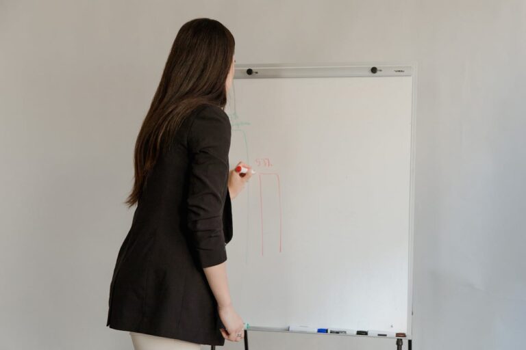 Female employee in black blazer writing on whiteboard during office meeting.